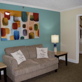 A cozy living room with a beige sofa, colorful abstract wall art, and a lamp on a side table.