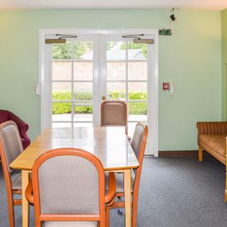 A cozy dining area with a wooden table, chairs, and large windows leading to the outside.
