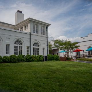 A scenic view of a white building with arched windows and a well-maintained lawn under a cloudy sky.