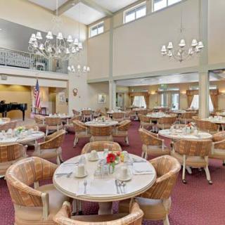 A spacious dining room with elegant chandeliers, round tables, and plush chairs.