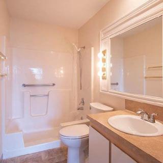 A bright bathroom with a shower, toilet, and sink beneath a large mirror.