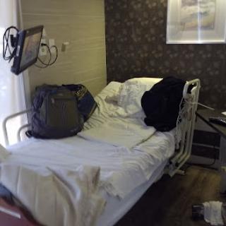 A hospital room prepared for a patient, featuring a bed with personal belongings nearby.