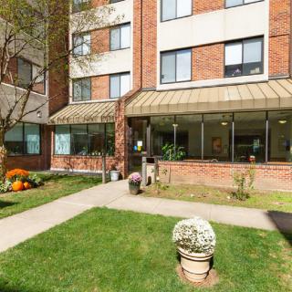 An exterior view of an apartment building with a well-maintained lawn and flower arrangements near the entrance.