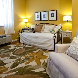 A cozy living room with yellow walls, featuring a daybed, patterned rug, and soft lighting from lamps.