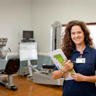 A healthcare professional smiles while holding a clipboard in a fitness clinic, showcasing a welcoming atmosphere.