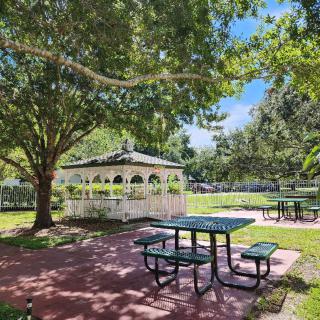 A serene park setting featuring a gazebo and picnic tables surrounded by lush trees on a sunny day.