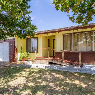 A yellow house with a ramp and a tree in the front yard under a clear blue sky.