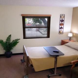 A cozy single bedroom with a window, bedside lamp, and an overbed table.