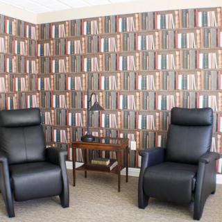 A cozy living room with two black recliners and a bookshelf-themed wallpaper.