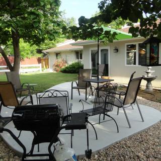 A cozy backyard patio with chairs and a table under a large tree, offering a comfortable outdoor seating area.