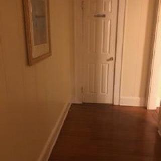 A quiet hallway with a wooden floor, white door, and framed picture hanging on the wall.