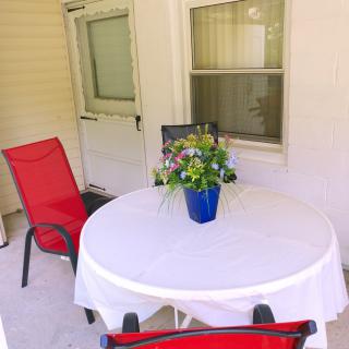 A cozy patio with a table set for relaxation, featuring red chairs and a floral centerpiece.