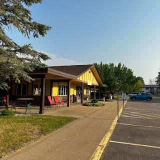 A charming yellow building with a welcoming porch, surrounded by trees and an empty parking lot.
