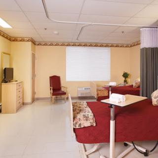A well-furnished patient room in a hospital, featuring two beds, a television, and comfortable seating.