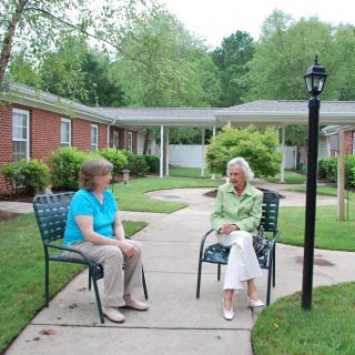 Two women sitting on chairs in a garden area engaged in conversation.