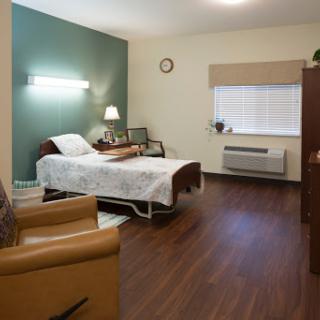 A well-furnished hospital patient room featuring a bed, chair, and natural light.