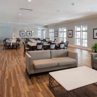 A spacious, modern lounge area featuring sofas, tables, and chairs on a wooden floor with bright lighting.