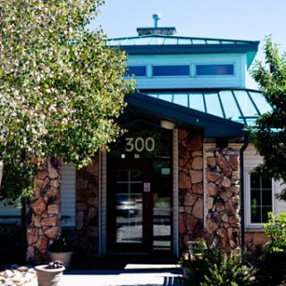 A modern building featuring a stone facade and a distinctive blue roof, surrounded by lush greenery.
