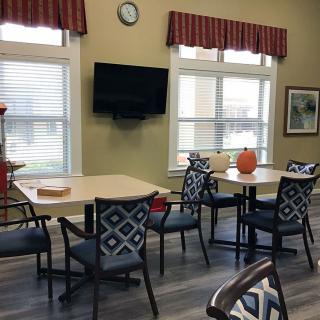 A cozy room with tables and chairs, featuring a wall-mounted television and large windows.