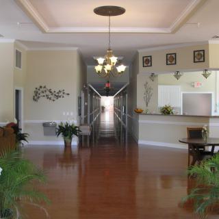 A spacious hallway with a chandelier and wooden flooring, adorned with plants and decorative elements.