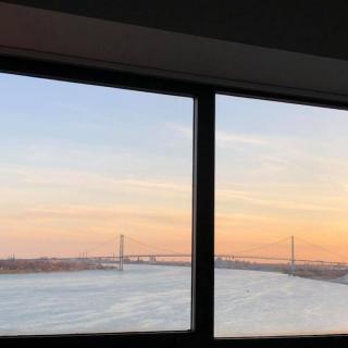 A scenic sunset view through a window, overlooking a river and bridge.