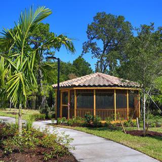 A scenic garden view featuring a gazebo with a tiled roof, surrounded by lush greenery and a winding pathway.