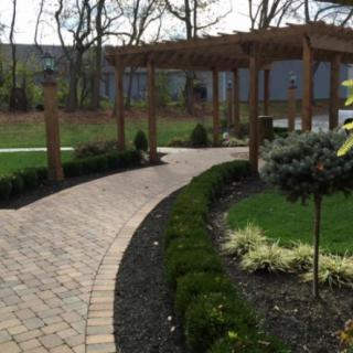 A beautifully landscaped garden path with a brick walkway leading to a wooden pergola.
