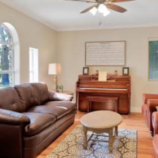 A cozy living room featuring a sofa, armchair, and piano, with a coffee table centered on a patterned rug.