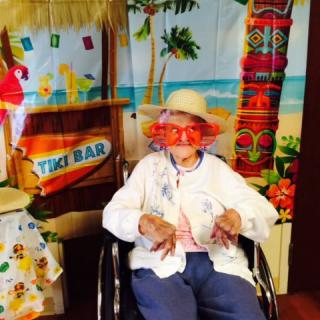 A person in a wheelchair is enjoying a tropical-themed event, wearing a hat and fun glasses.