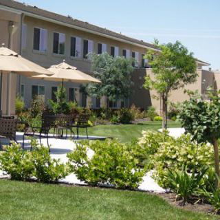 A landscaped outdoor patio area with benches, tables, and umbrellas near a building.