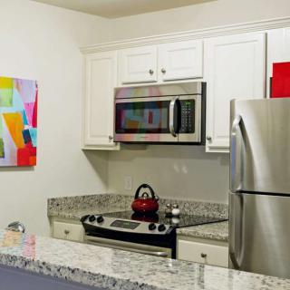A modern kitchen with stainless steel appliances and granite countertops, featuring colorful artwork on the wall.