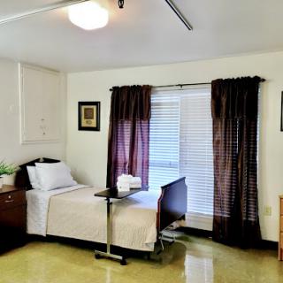 A cozy hospital room featuring a single bed, bedside table, and natural light filtering through the curtains.