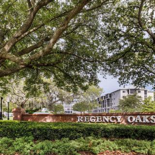 Entrance sign of the Regency Oaks apartment complex surrounded by lush trees and greenery.