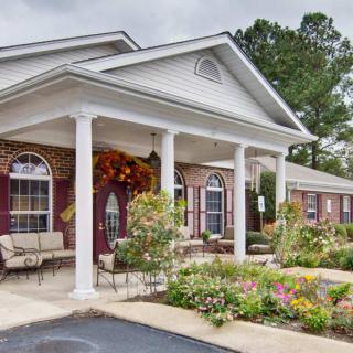 A well-maintained building with a garden in front and a welcoming porch supported by columns.
