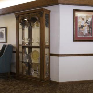 A cozy interior featuring a wooden display cabinet filled with decorative items, alongside framed art on the walls and an upholstered chair.
