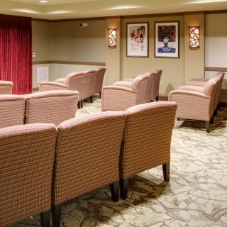 A cozy theater-style room with rows of upholstered chairs facing a screen, adorned with wall art and warm lighting.