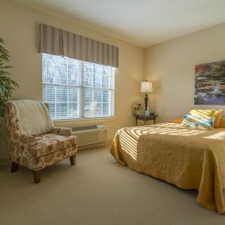 A cozy bedroom with a bed, chair, and a large window allowing natural light.