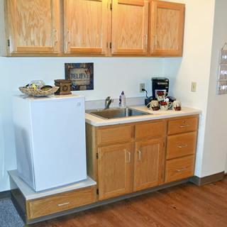 A compact kitchenette with a mini fridge, sink, and wooden cabinets.