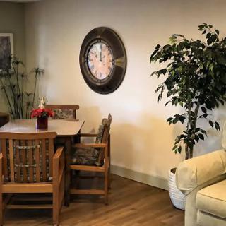 A cozy living room corner with wooden furniture, a dining table, chairs, an indoor plant, and a wall clock.