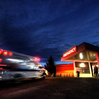 An ambulance rushes towards the emergency department of a hospital during the evening.