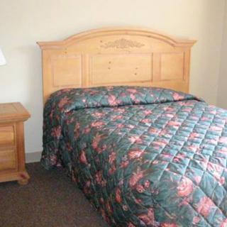 A bedroom with a wooden headboard, floral quilt, and a matching nightstand.