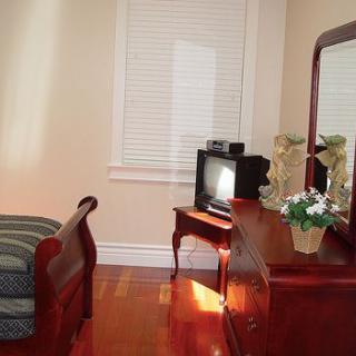 A cozy bedroom with a bed, wooden dresser with a mirror, and a small TV on a stand.