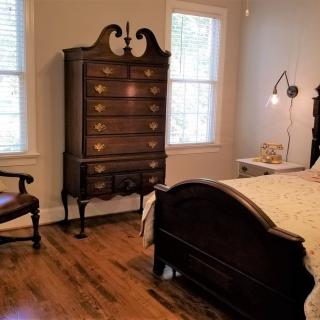 A cozy bedroom featuring vintage furniture with a dark wooden bed, an ornate chest of drawers, and elegant wooden flooring.