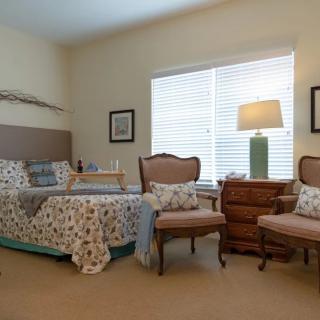 A cozy bedroom with a bed, chairs, and a lamp near a window.