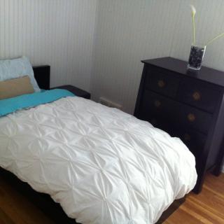 A minimalist bedroom with a single bed and a dark wooden dresser.