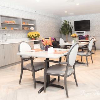 A modern dining area featuring elegant tables and chairs, decorated with fresh flowers and a wall-mounted television.