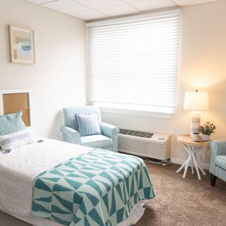 A cozy bedroom with a single bed, two armchairs, and a warm lamp by the window.