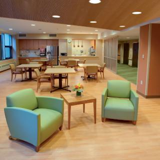 A modern lounge area featuring comfortable green chairs and a wooden table, designed for relaxation and social interaction.