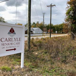 A sign indicating the direction to Carlyle Senior Care amidst a rural backdrop.