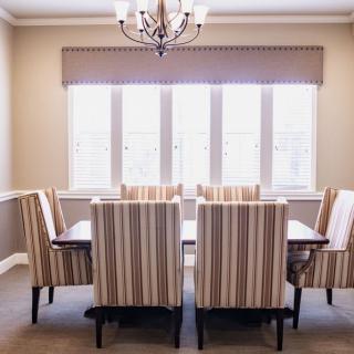A dining room with a set of six striped upholstered chairs around a wooden table, illuminated by a chandelier and natural light from the window.